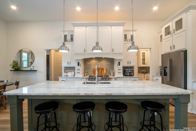 kitchen with high quality fridge, hanging light fixtures, white cabinets, and a spacious island