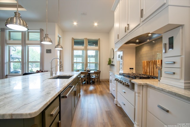 kitchen featuring backsplash, wood-type flooring, white cabinetry, hanging light fixtures, and an island with sink