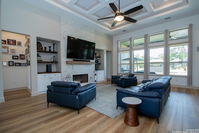 living room featuring ceiling fan, light wood-type flooring, a fireplace, and coffered ceiling