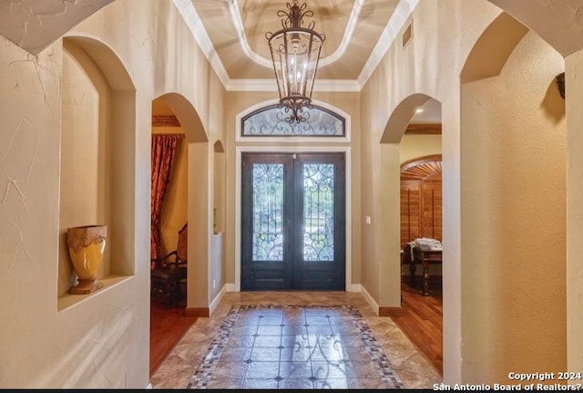 entryway with french doors, ornamental molding, a raised ceiling, hardwood / wood-style flooring, and a chandelier