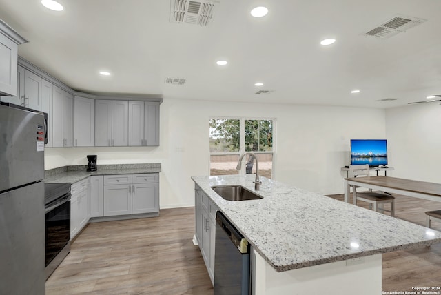 kitchen with light stone countertops, sink, stainless steel appliances, light hardwood / wood-style flooring, and a center island with sink