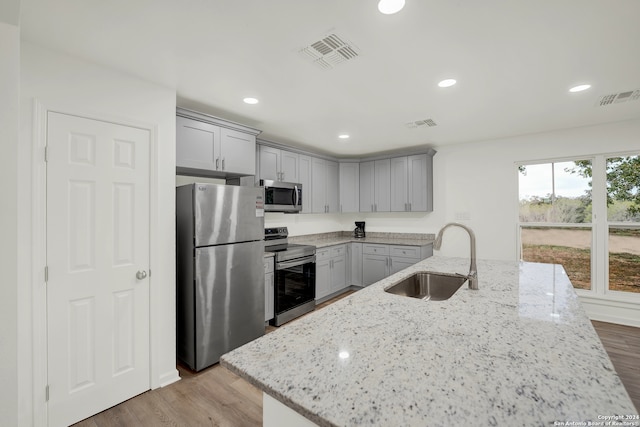 kitchen with light stone countertops, sink, stainless steel appliances, and light hardwood / wood-style flooring