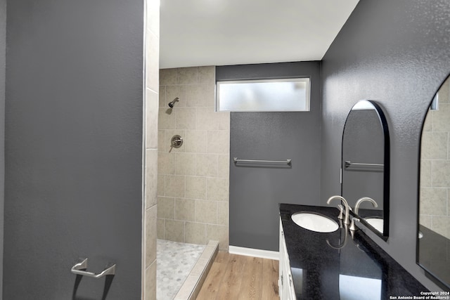 bathroom with a tile shower, vanity, wood-type flooring, and vaulted ceiling