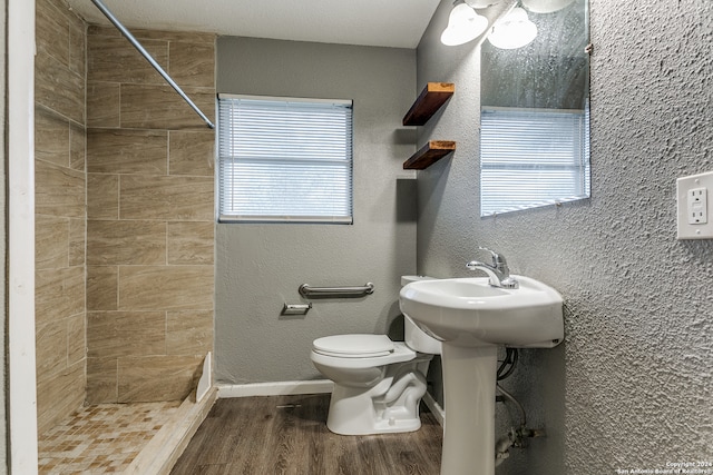 bathroom featuring hardwood / wood-style floors, a tile shower, toilet, and a wealth of natural light