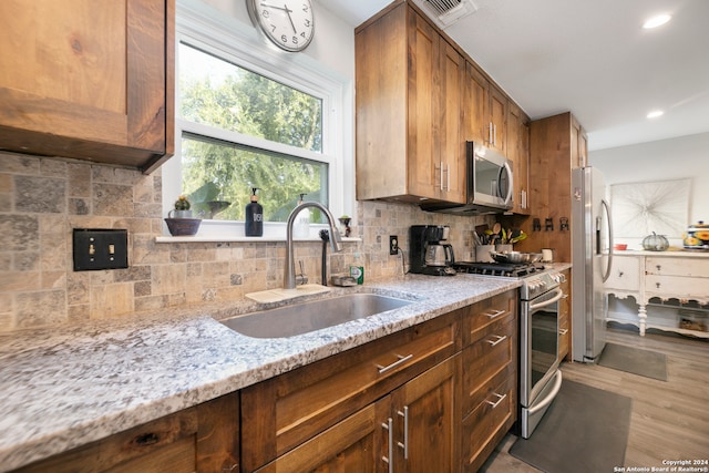 kitchen with sink, decorative backsplash, light hardwood / wood-style floors, light stone counters, and stainless steel appliances