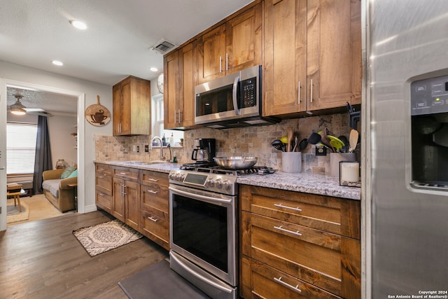 kitchen featuring sink, stainless steel appliances, tasteful backsplash, light stone counters, and dark hardwood / wood-style flooring