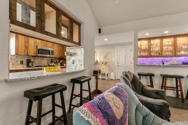 bar featuring light stone countertops, backsplash, vaulted ceiling, and dark wood-type flooring