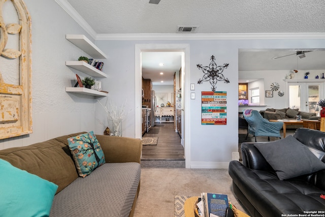 carpeted living room featuring ceiling fan, ornamental molding, and a textured ceiling