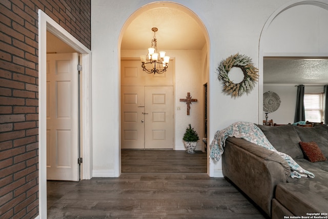 foyer featuring dark wood-type flooring, brick wall, and a chandelier