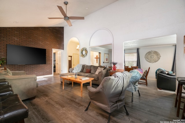 living room featuring high vaulted ceiling, ceiling fan, dark wood-type flooring, and brick wall