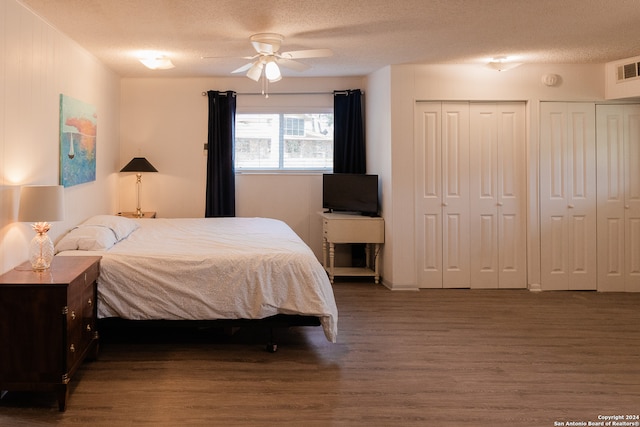 bedroom featuring ceiling fan, dark hardwood / wood-style flooring, a textured ceiling, and multiple closets