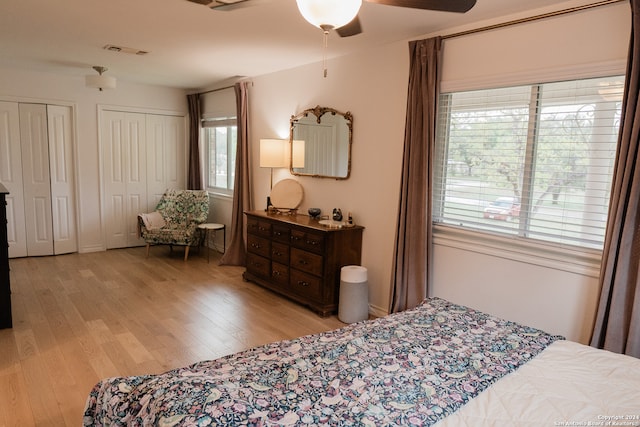 bedroom with ceiling fan, light hardwood / wood-style flooring, and two closets