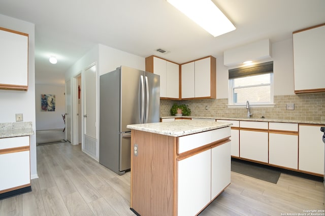 kitchen with sink, stainless steel fridge, a kitchen island, light hardwood / wood-style floors, and white cabinetry