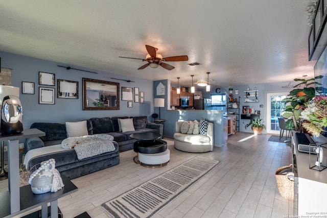 living room with a textured ceiling, light hardwood / wood-style floors, and ceiling fan