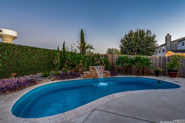 pool at dusk featuring pool water feature