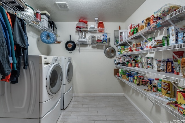 laundry area with light wood-type flooring, a textured ceiling, and washing machine and clothes dryer