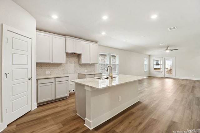 kitchen featuring sink, white cabinets, backsplash, hardwood / wood-style flooring, and a kitchen island with sink