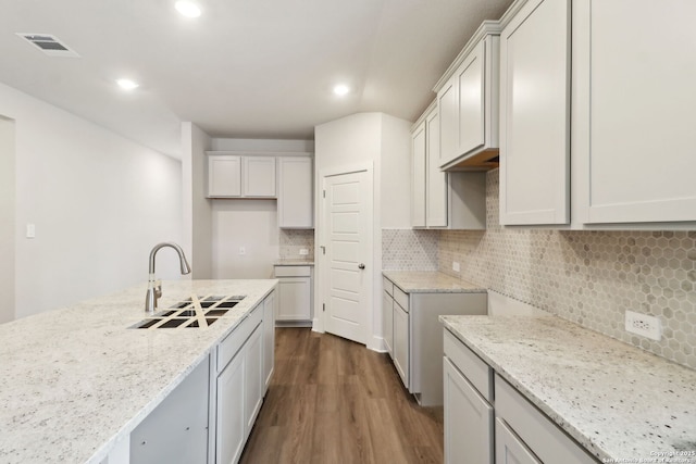 kitchen featuring sink, white cabinetry, dark hardwood / wood-style flooring, light stone countertops, and decorative backsplash