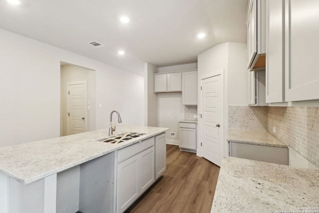 kitchen with dark wood-type flooring, sink, light stone counters, white cabinetry, and decorative backsplash