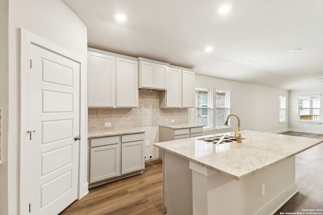 kitchen featuring hardwood / wood-style flooring, white cabinetry, a kitchen island with sink, and sink