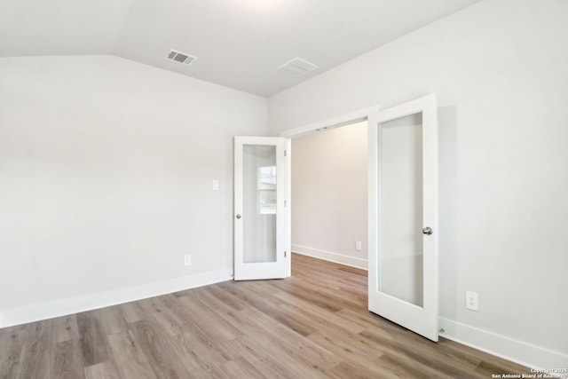 unfurnished bedroom featuring french doors, vaulted ceiling, and light hardwood / wood-style floors