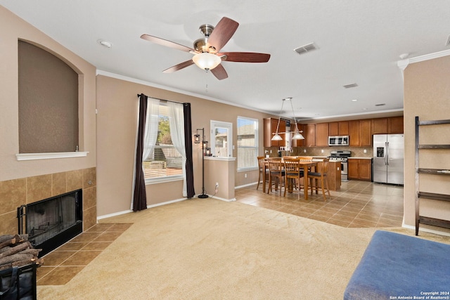 carpeted living room with a tiled fireplace, ceiling fan, and ornamental molding