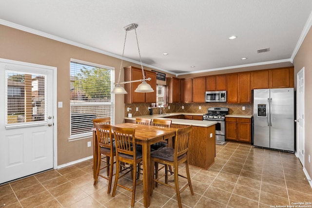 kitchen with tasteful backsplash, tile patterned floors, ornamental molding, stainless steel appliances, and pendant lighting