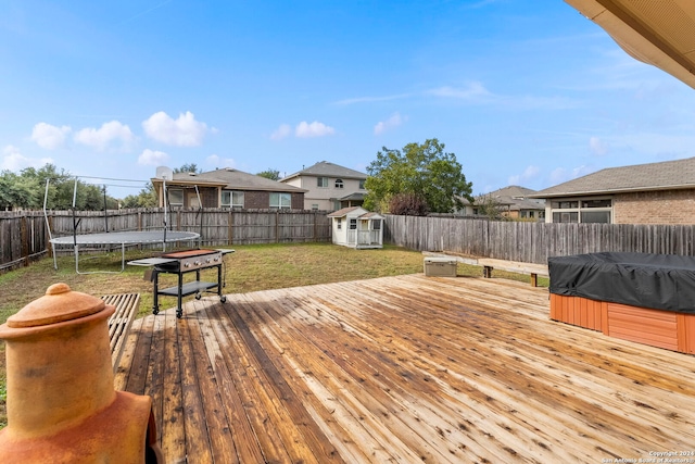 deck with a lawn, an outdoor structure, a hot tub, and a trampoline