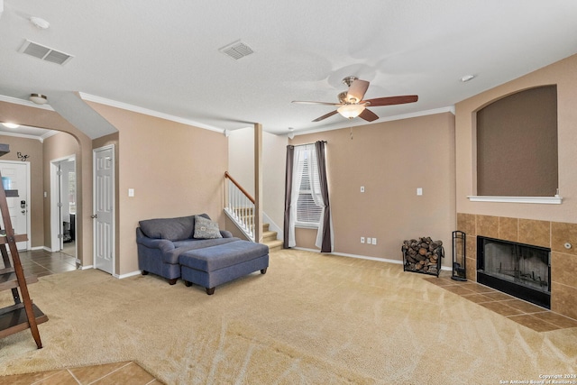 living area featuring carpet flooring, ceiling fan, crown molding, and a tiled fireplace