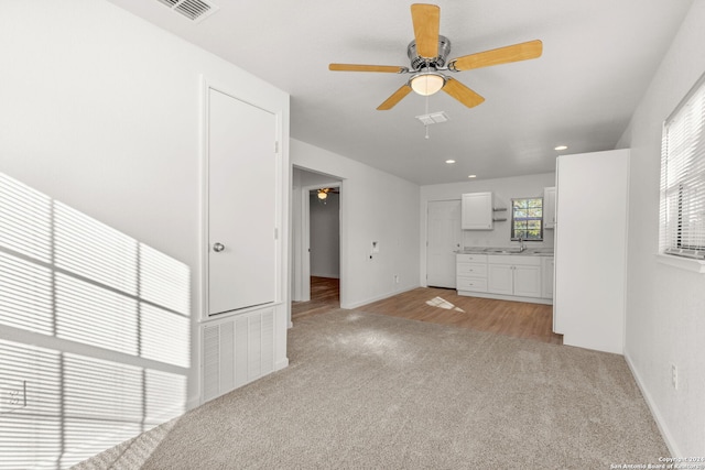 unfurnished living room featuring light carpet, ceiling fan, and sink