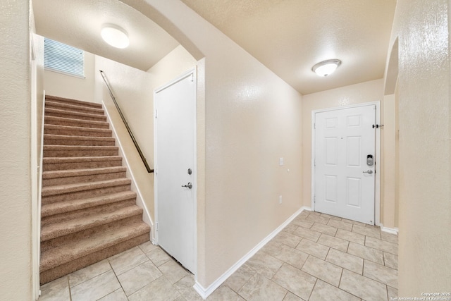 entryway with baseboards, stairs, light tile patterned floors, arched walkways, and a textured ceiling