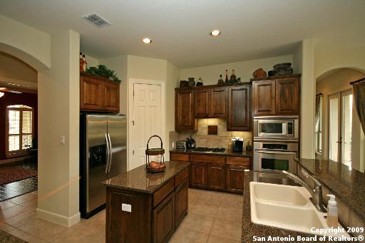 kitchen with appliances with stainless steel finishes, tasteful backsplash, sink, light tile patterned floors, and a center island with sink