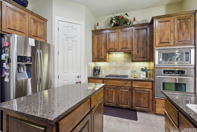 315 Dona Ana Cv, Helotes, TX 78023 - kitchen with appliances with stainless steel finishes, decorative backsplash, dark stone countertops, light tile patterned floors, and a center island
