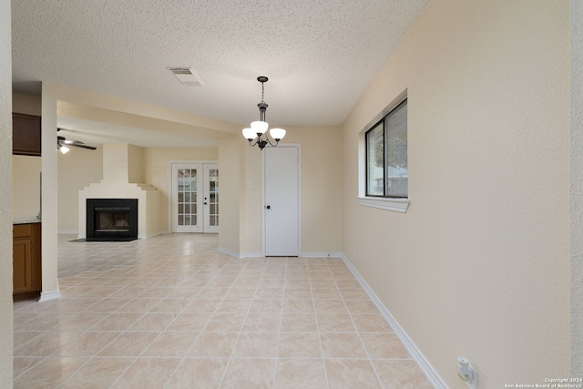 unfurnished living room featuring french doors, ceiling fan with notable chandelier, light tile patterned floors, a textured ceiling, and a large fireplace