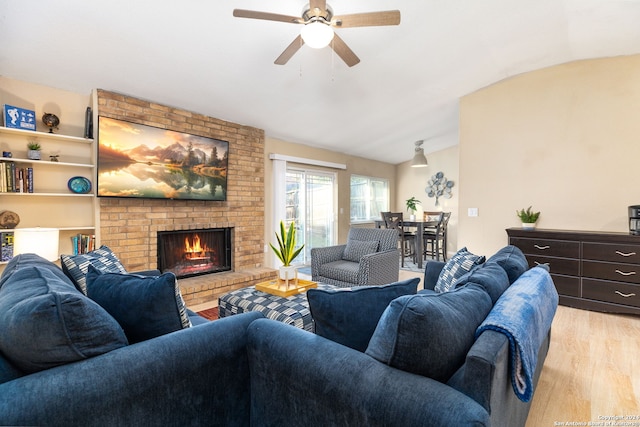 living room featuring ceiling fan, light hardwood / wood-style floors, vaulted ceiling, and a brick fireplace