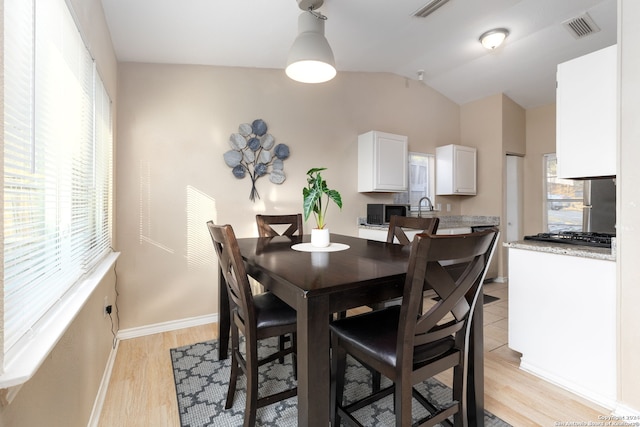 dining room featuring light wood-type flooring, vaulted ceiling, and sink