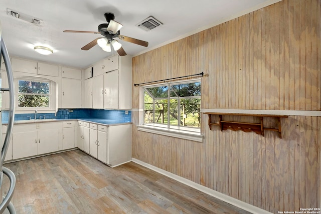 kitchen with wood walls, white cabinets, light hardwood / wood-style floors, and ceiling fan