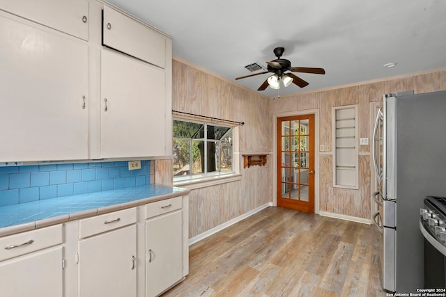 kitchen featuring white cabinets, stainless steel fridge, wood walls, and light wood-type flooring