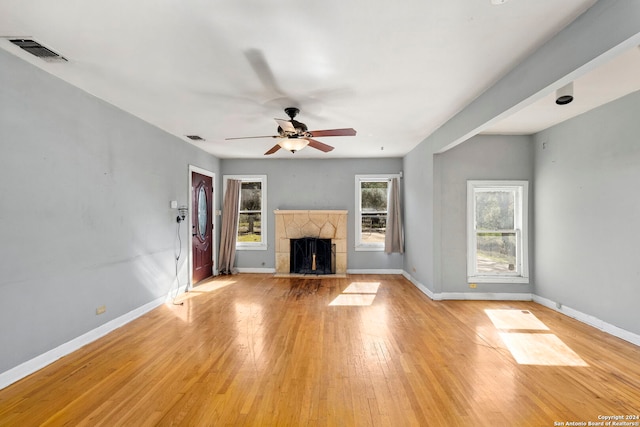 unfurnished living room featuring light wood-type flooring, ceiling fan, and a tiled fireplace