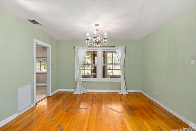 empty room featuring wood-type flooring, an inviting chandelier, and plenty of natural light