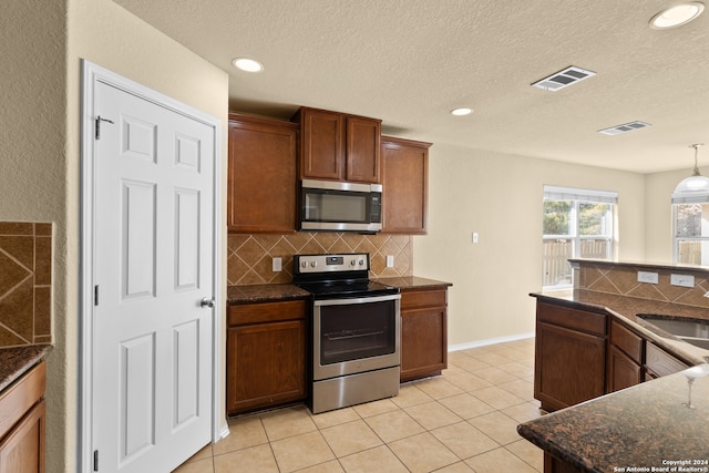 kitchen featuring a textured ceiling, appliances with stainless steel finishes, tasteful backsplash, decorative light fixtures, and light tile patterned flooring