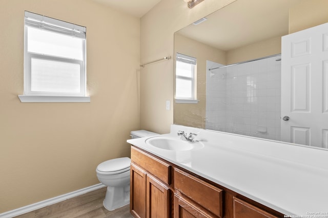 bathroom with hardwood / wood-style flooring, vanity, toilet, and a tile shower