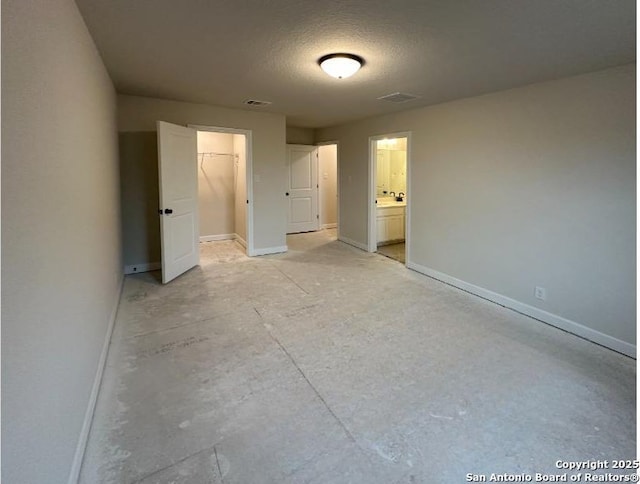 unfurnished bedroom with a spacious closet, a closet, ensuite bathroom, and a textured ceiling