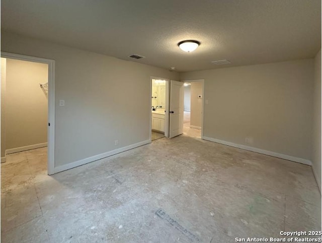 unfurnished bedroom with a textured ceiling, a closet, a spacious closet, and ensuite bath