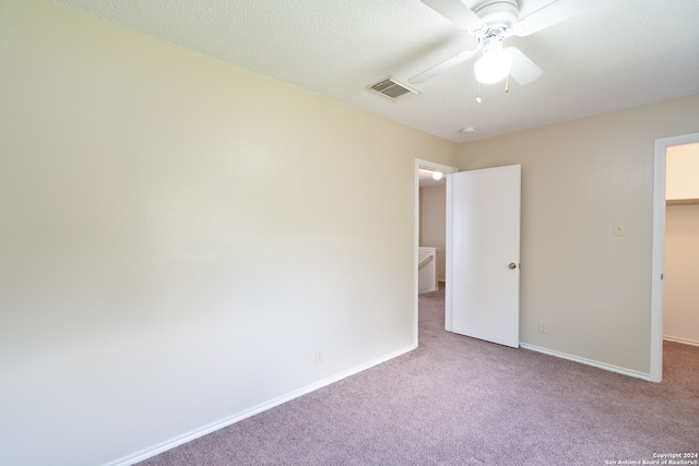 unfurnished bedroom featuring ceiling fan, light colored carpet, a textured ceiling, a walk in closet, and a closet