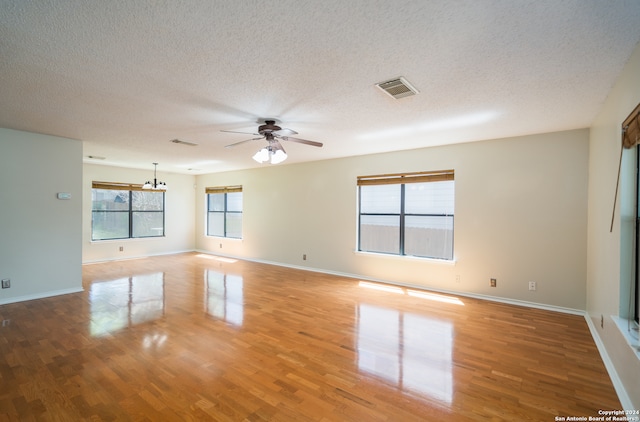 empty room featuring ceiling fan with notable chandelier, a textured ceiling, and wood-type flooring