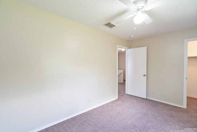 unfurnished bedroom with a spacious closet, a textured ceiling, a closet, carpet flooring, and ceiling fan