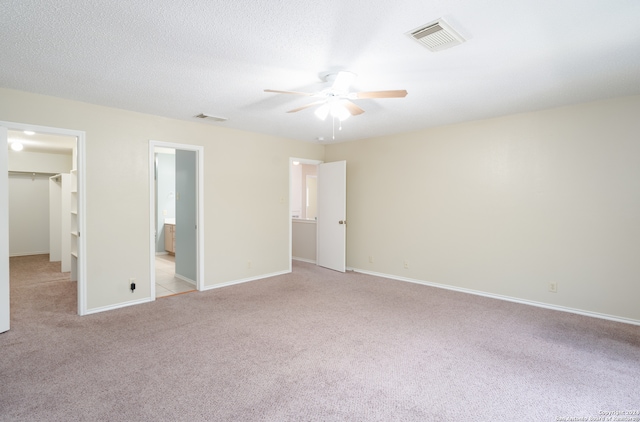 unfurnished bedroom with ensuite bathroom, a walk in closet, light carpet, a closet, and ceiling fan