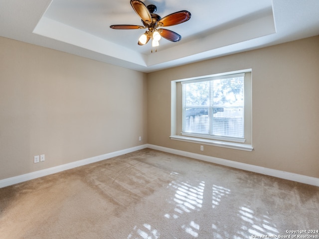 unfurnished room featuring light carpet, a tray ceiling, and ceiling fan