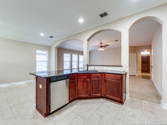 kitchen with stainless steel dishwasher, dark stone counters, ceiling fan, sink, and a center island with sink